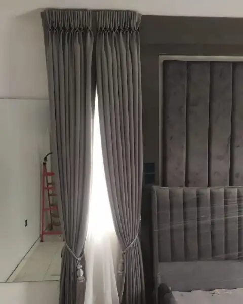Grey pinch-pleat curtains beside an upholstered bed