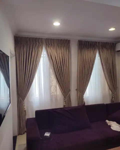 Bronze pinch-pleat curtains behind a plum sofa